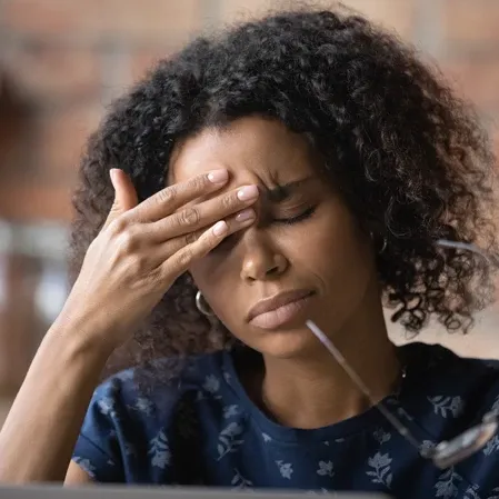 Person touching the forehead while seated at a desk, representing tension headaches and daily stress.